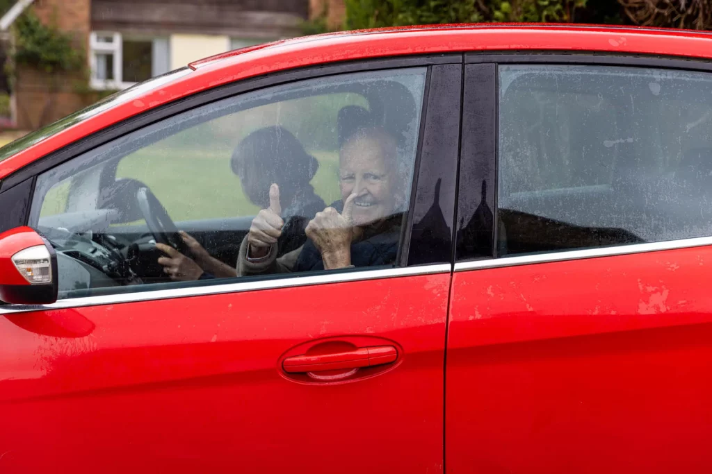 Smiling older man giving a thumbs-up from a red car
