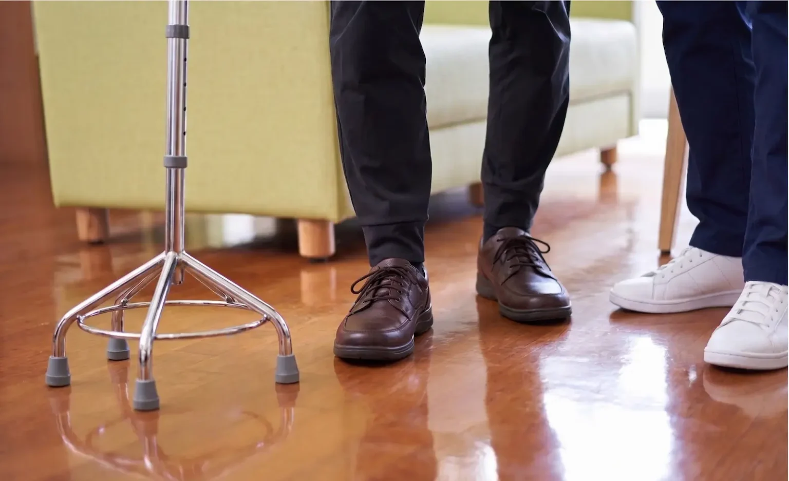 Older man taking a step with a quad stick while a physiotherapist stands close by to support him at home