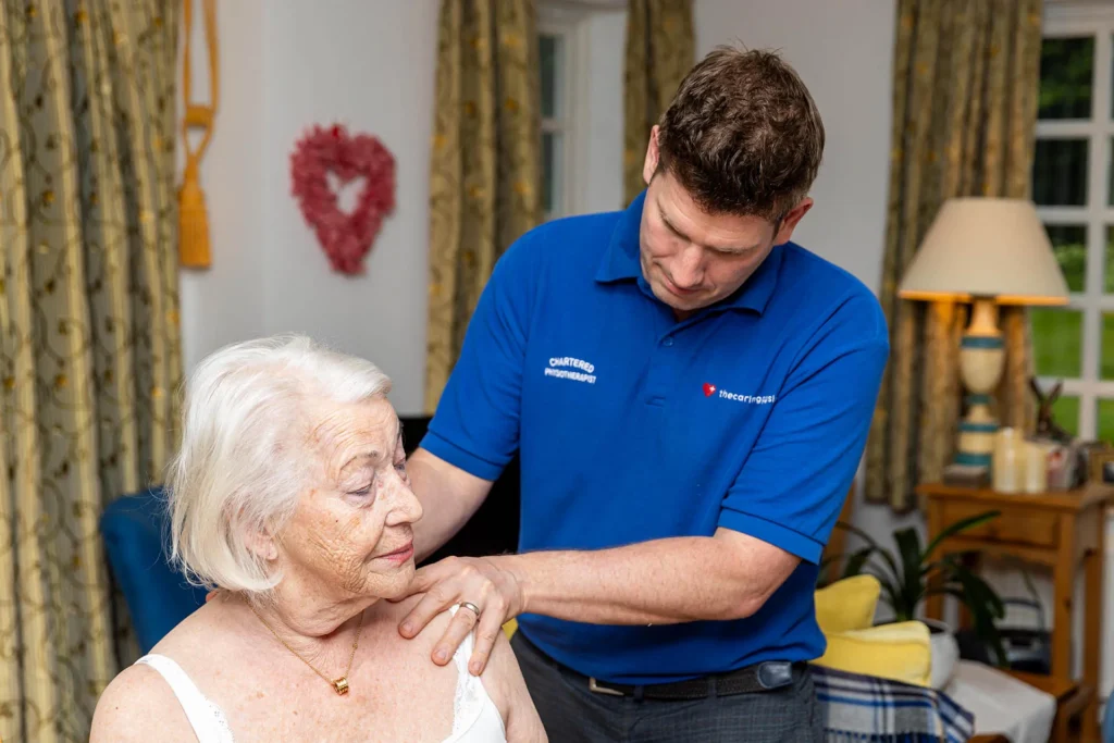Physiotherapist with his hand on an older woman's shoulder during a home visit in her sitting room