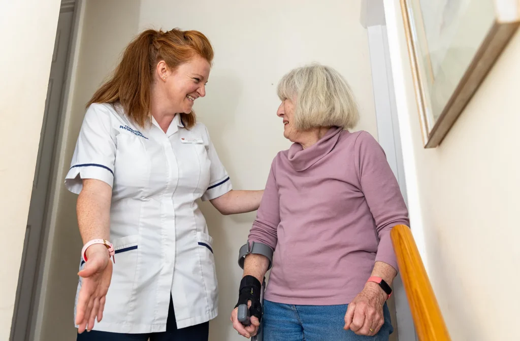 A physiotherapist supporting an older woman as she climbs the stairs at home