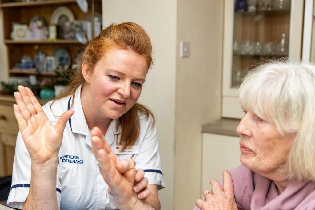 A physiotherapist explaining an exercise to an older woman, using her hands to demonstrate