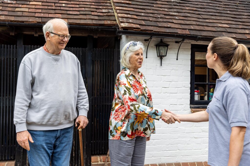 A physiotherapist shaking hands with an older woman at the front door, with her husband beside her