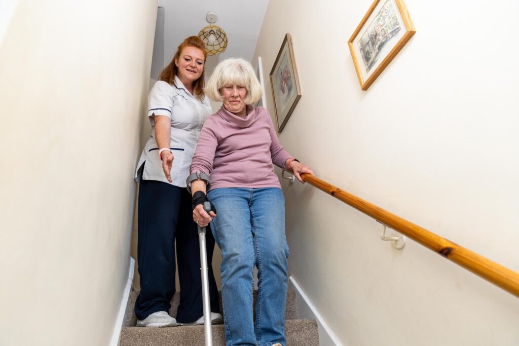 A physiotherapist beside an older woman as she practises coming down the stairs holding the handrail