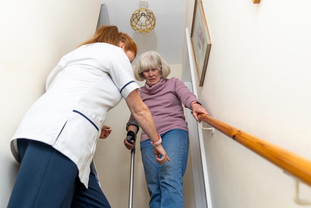 A physiotherapist supporting an older woman as she climbs the stairs using the handrail